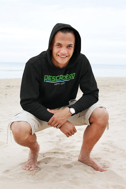 Man kneeling down smiling at the beach wearing a hooded sweatshirt with original Pescadero design printed across the chest