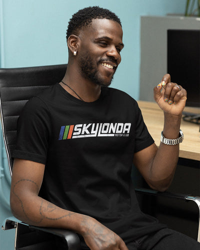Man sitting at a desk wearing a short sleeve t-shirt with "Sky Londa Motor Club" Rally logo printed across the chest