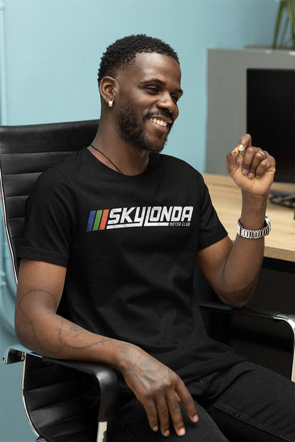 Man sitting at a desk wearing a short sleeve t-shirt with "Sky Londa Motor Club" Rally logo printed across the chest